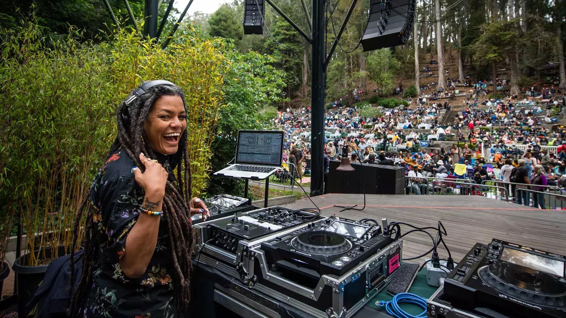 在Stern Grove Festival当DJ的一位女性，肩膀后面对着镜头微笑着.