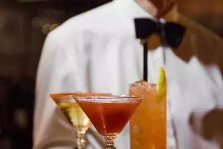 Un cameriere con indosso un papillon presenta un vassoio di cocktail all'Absinthe Restaurant di San Francisco.
