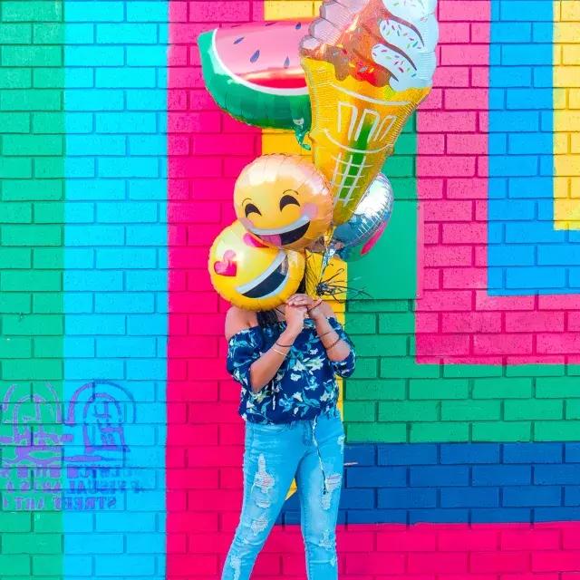 Una ragazza festeggia il suo compleanno con palloncini davanti a un murale colorato.