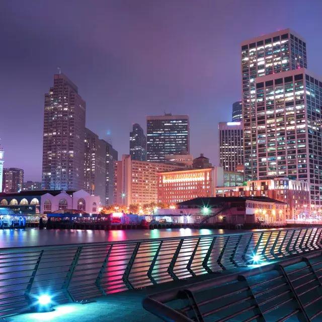 San Francisco's Embarcadero is lit up at night in an array of pastel colors.